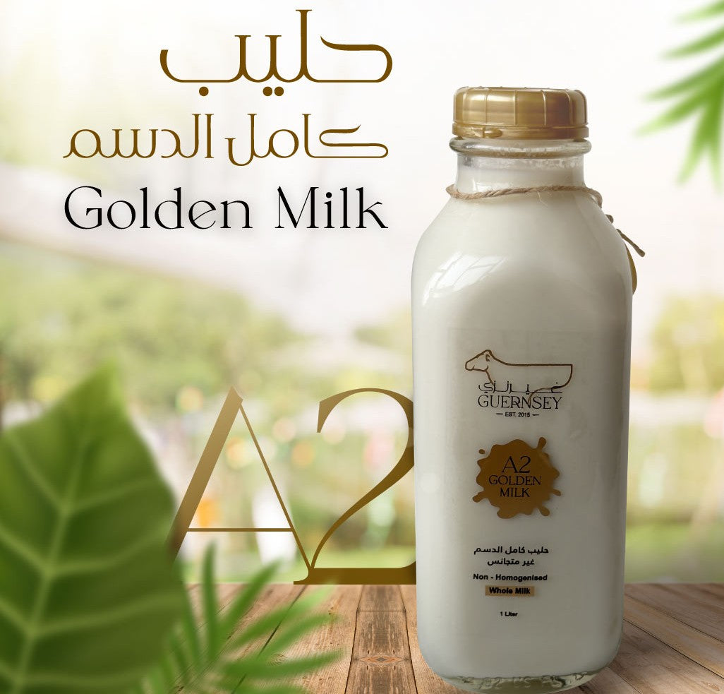 A bottle of Golden Milk (A2 Golden Milk) by Guernsey, shown on a wooden surface with a blurred green garden background. The bottle is filled with white milk and has a gold cap, with gold and black branding on the label.