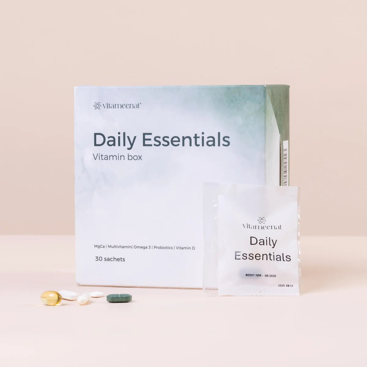 Vlaneena Daily Essentials Vitamin box packaging with a white box and sachet, alongside three loose capsules on a light beige background.