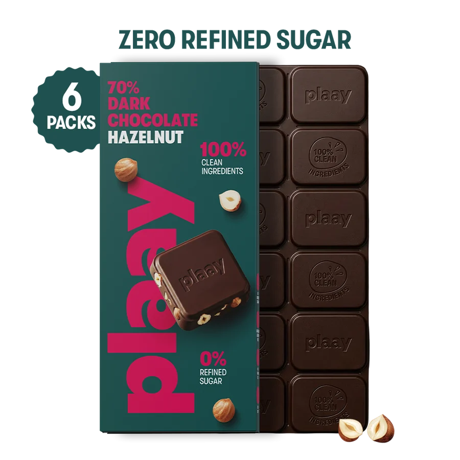 A retail package of plaay chocolate hazelnut bars shown on a white background, with a dark teal box labeled 'ZERO REFINED SUGAR', '70% DARK CHOCOLATE HAZELNUT', and '6 PACKS', alongside a chocolate bar and two hazelnut halves.
