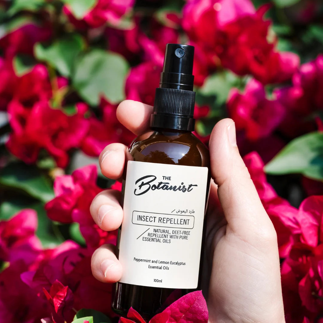 Hand holding a bottle of 'The Botanist' insect repellent against a floral background