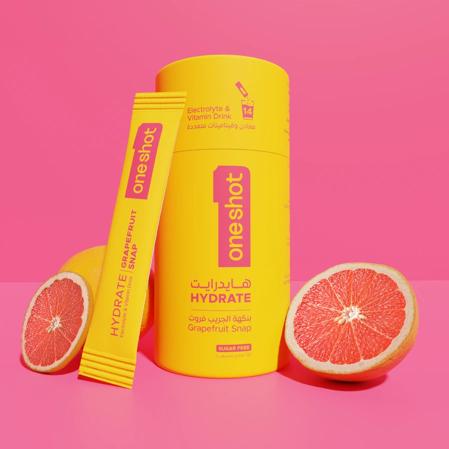 A bright yellow OneShot Hydrate grapefruit slimming strip product set, featuring a cylindrical container, a single wrapped strip, and two sliced grapefruit halves on a solid pink background.