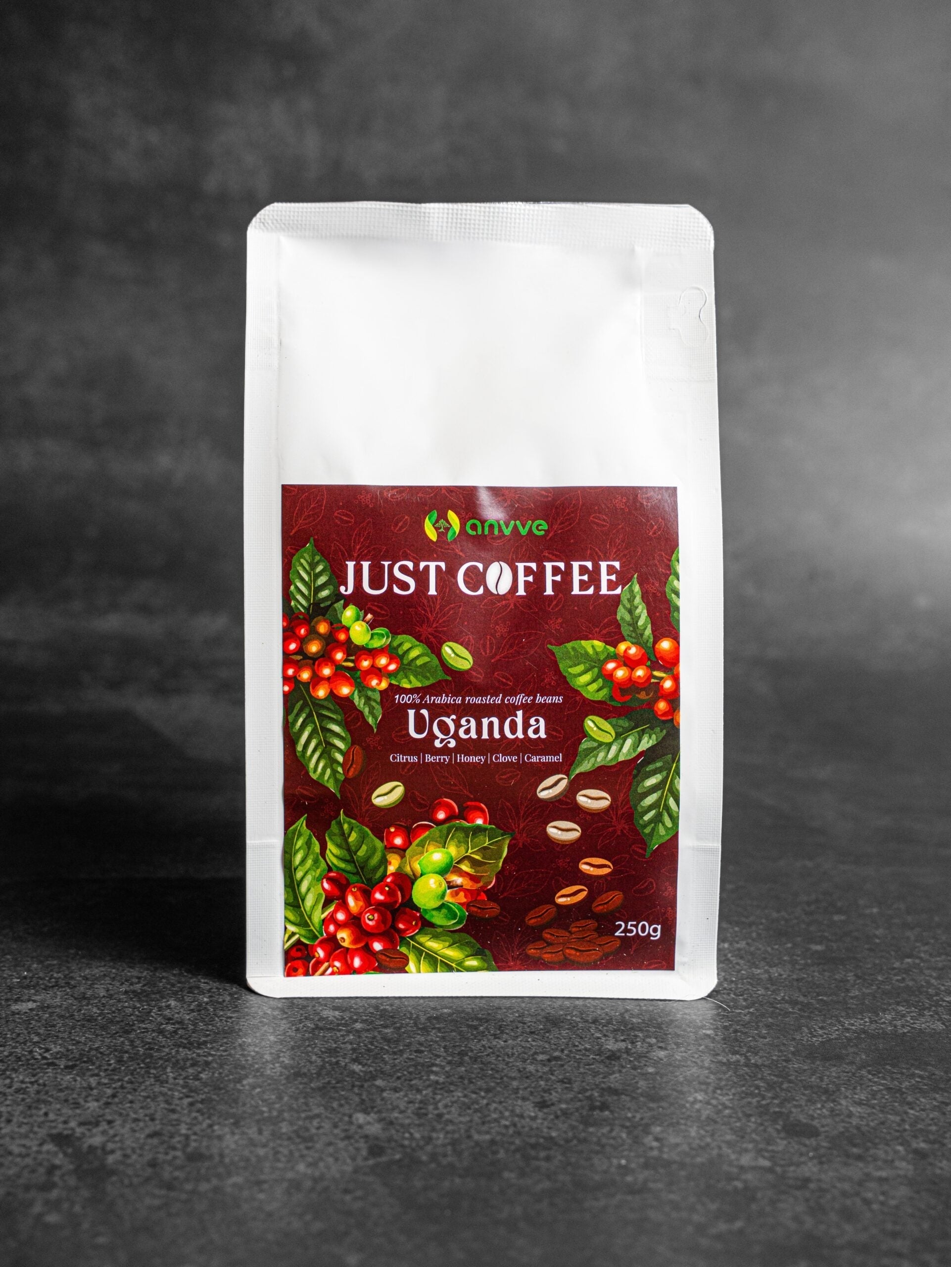 A stand-up pouch of Just Coffee Uganda whole bean coffee, featuring a white package with a prominent dark red label decorated with coffee cherries and leaves, set against a dark gray textured background.