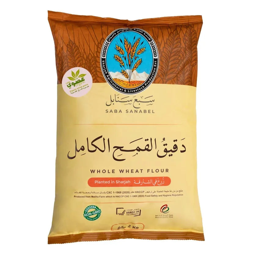A 2 kg bag of Saba Sanabel Whole Wheat Flour, featuring a cream-colored lower half and a brown upper half with wheat illustrations. The packaging includes the Saba Sanabel logo, a 'Planted in Shagab' badge, and various certification logos.