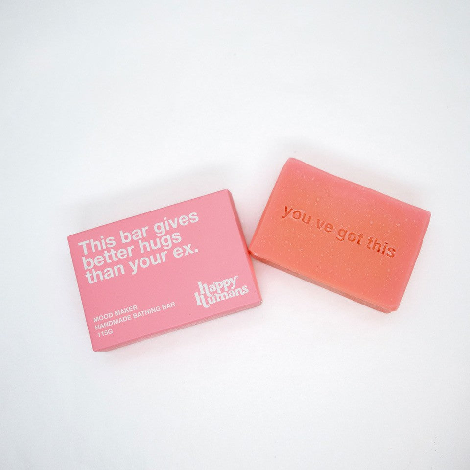 Two pink rectangular bars of handmade bath bar with embossed text, shown on a clean white background. One bar is wrapped in pink paper with white text reading 'This bar gives better hugs than your ex.