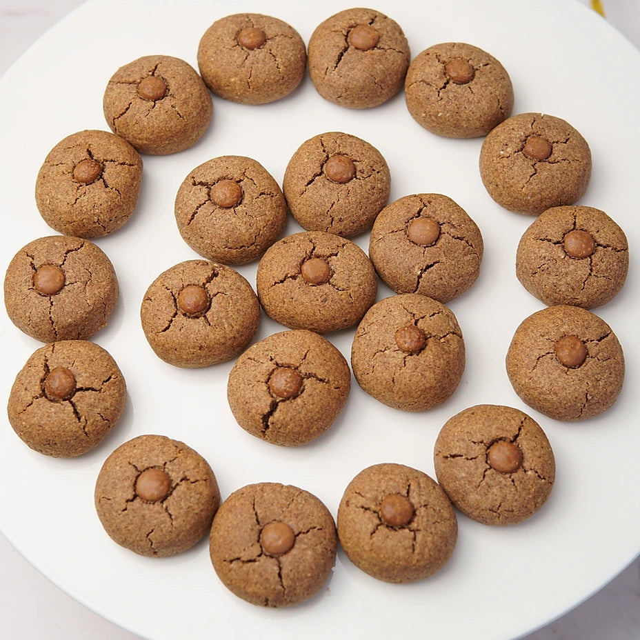 A set of round brown cookies arranged in a circle on a white plate, each topped with a small chocolate piece in the center.
