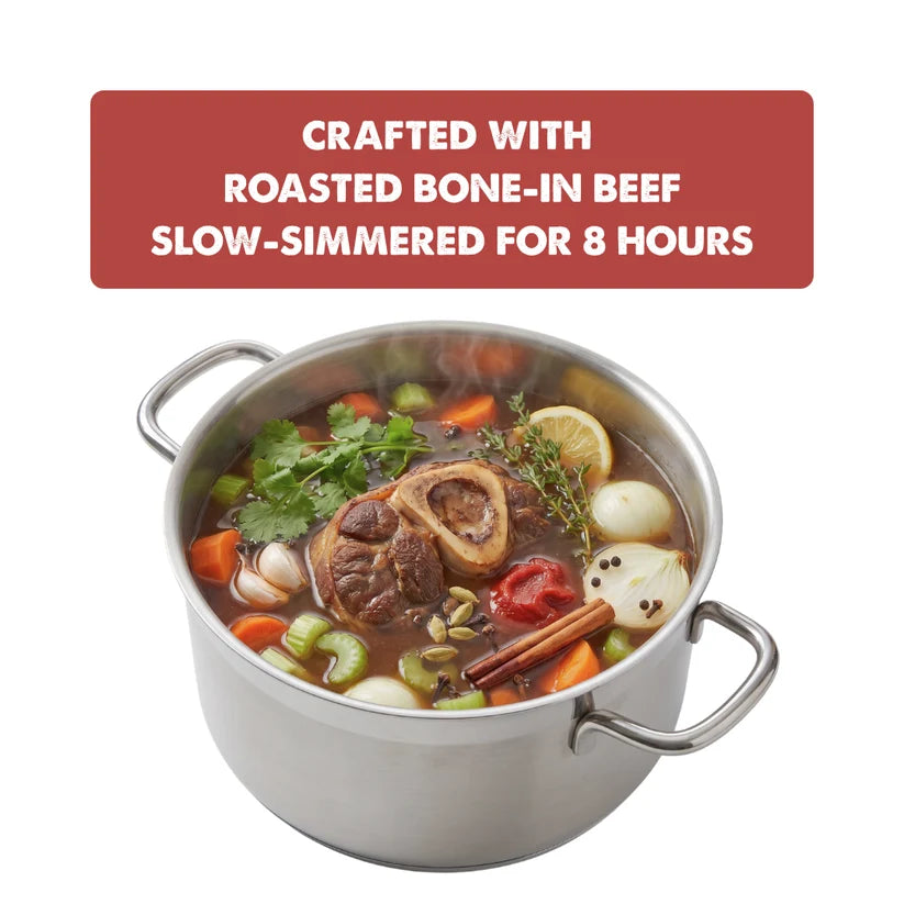 A stainless steel pot filled with a hearty bone-in beef stew, featuring carrots, celery, lemons, herbs, and spices, with a red text banner at the top reading 'CRAFTED WITH ROASTED BONE-IN BEEF SLOW-SIMMERED FOR 8 HOURS'.