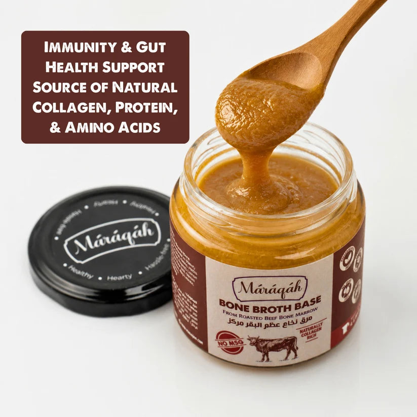 An open jar of Mārāqah Bone Broth Base with a wooden spoon lifting thick golden-brown broth above it, alongside the black branded lid and a text callout on a clean white background.