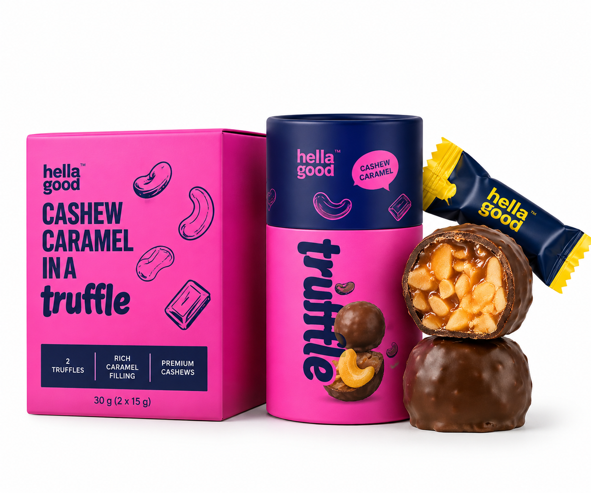 Hella Good Cashew Caramel in a Truffle chocolate set, featuring a bright pink box, a matching pink and navy cylindrical tin, a wrapped candy bar, and two chocolate truffles (one whole and one cut open to show the cashew caramel filling), all on a clean white background.