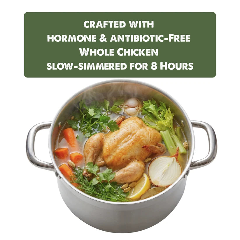 A stainless steel stockpot filled with a whole roasted chicken and vegetables, including carrots, celery, parsley, and onion, with steam rising. A dark green text banner at the top reads: 'CRAFTED WITH HORMONE & ANTIBIOTIC-FREE WHOLE CHICKEN SLOW-SIMMERED FOR 8 HOURS'.