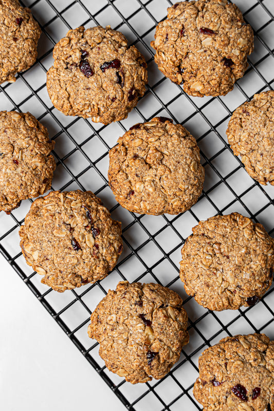 Oatmeal cookies with dried fruit pieces cooling on a black wire rack over a white surface.