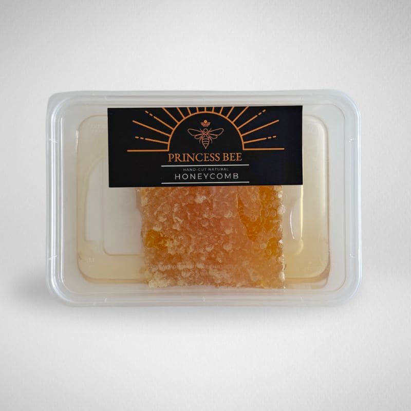 A clear plastic container holding a piece of honeycomb with amber-orange wax, sealed with a black label that reads Princess Bee Honeycomb.