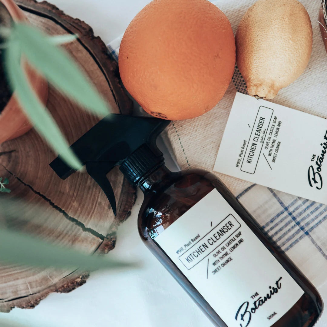 Bottle of 'The Botanist' kitchen cleanser with a sponge and lemon on a wooden surface.