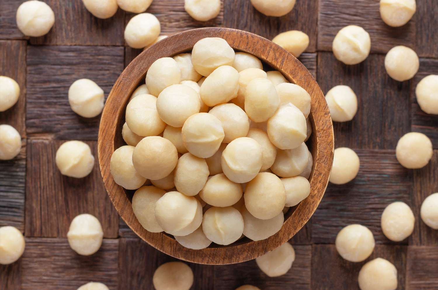 Wooden bowl filled with macadamia nuts on a wooden surface