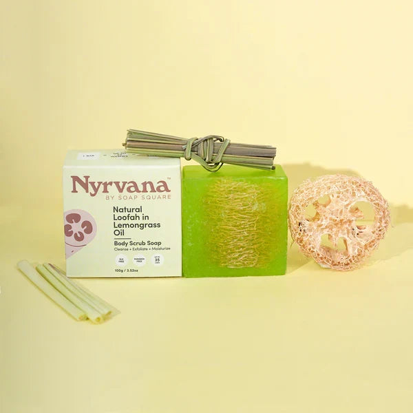 Nyrvana by Soap Square Natural Loaffish in Lemongrass Oil Body Scrub Soap, shown with a white branded box, a bright green rectangular bar of soap wrapped with a silver string, a pink soap sponge, and two pale yellow lemongrass sticks on a pale yellow background.