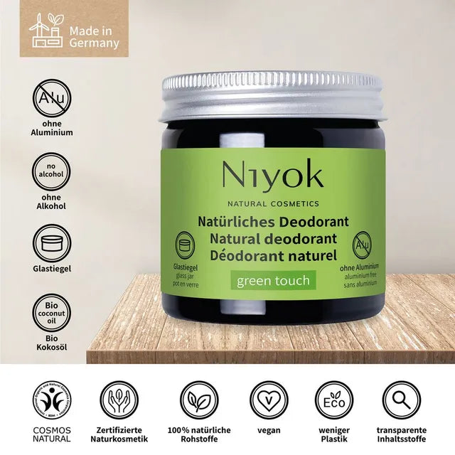 A jar of Niyok Natural Cosmetics 'green touch' natural deodorant, displayed on a wooden surface with various German certification and feature icons on both sides.