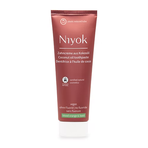 A tube of Niyok Coconut Oil Toothpaste in the 'blood orange & basil' scent, featuring a deep reddish-brown packaging with white text and a small green accent band at the bottom, set against a plain white background.