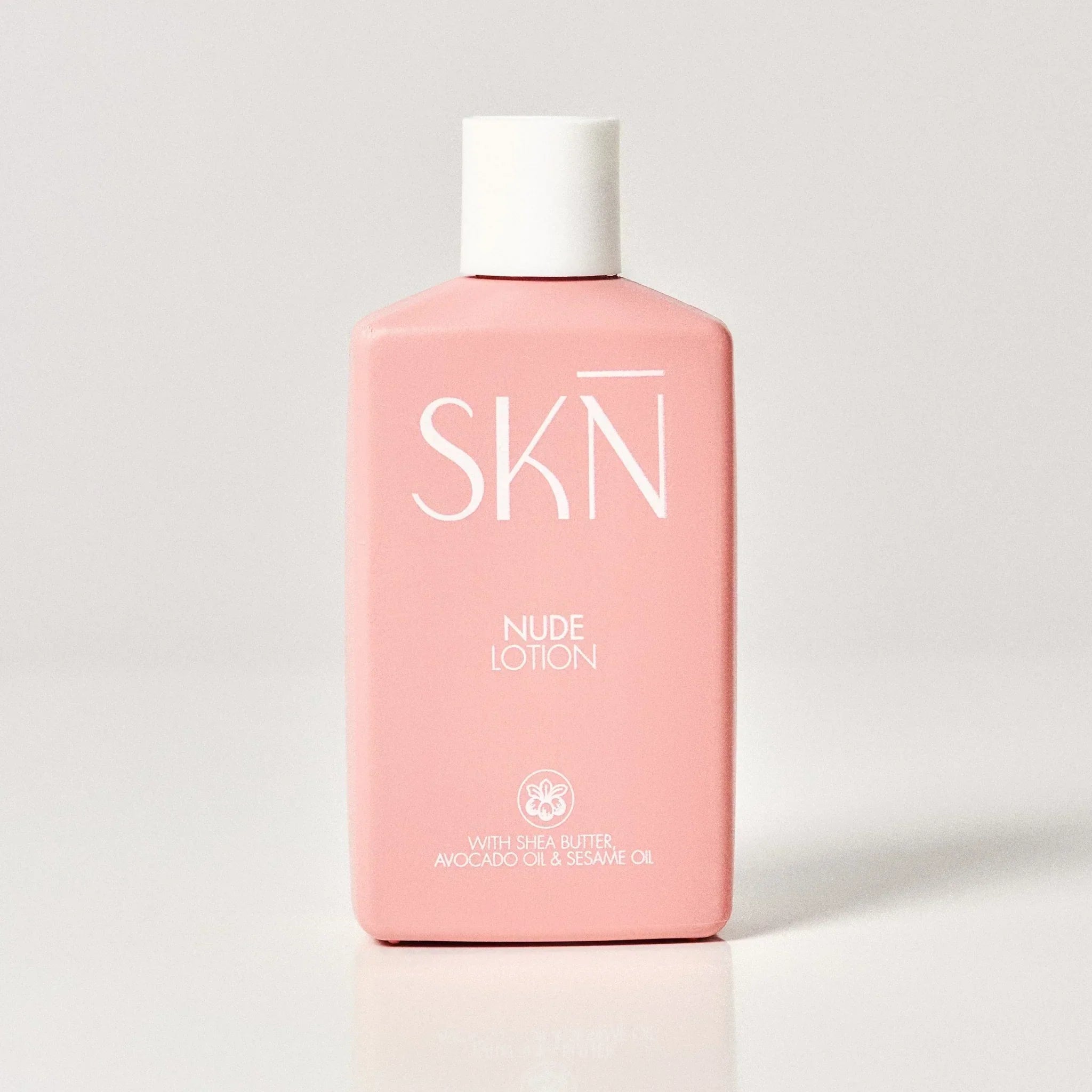A pink bottle of SKN Nude Lotion with a white cap, standing upright on a light gray reflective surface.