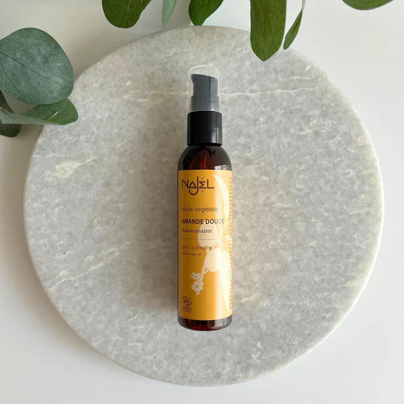 A bottle of Najel almond sourdough bread starter liquid culture, placed on a round white marble tray with green leaves in the background.
