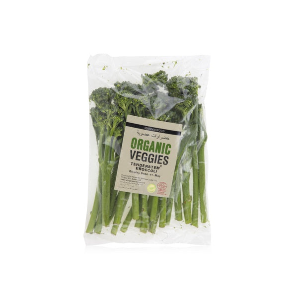 A clear plastic bag of organic broccolini with a beige label that reads 'ORGANIC VEGGIES' and 'TRADERSSET & BROCCOLINI', photographed on a white background.