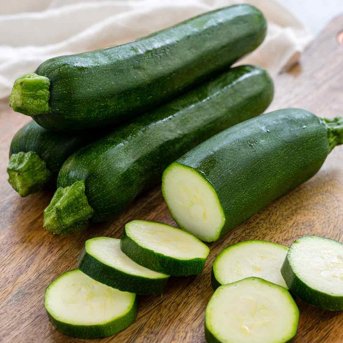 Zucchinis on a wooden cutting board with some sliced zucchinis.