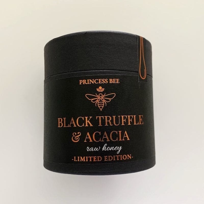 A black cylindrical tin of Princess Bee Black Truffle & Acacia raw honey, limited edition, on a plain off-white background.