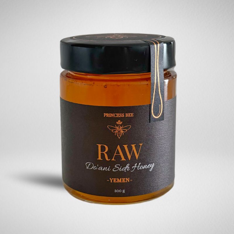 A glass jar of raw honey with a black lid and a dark brown label reading 'PRINCESS BEE RAW Do'ani Sidi Honey - YEMEN - 200 g'.