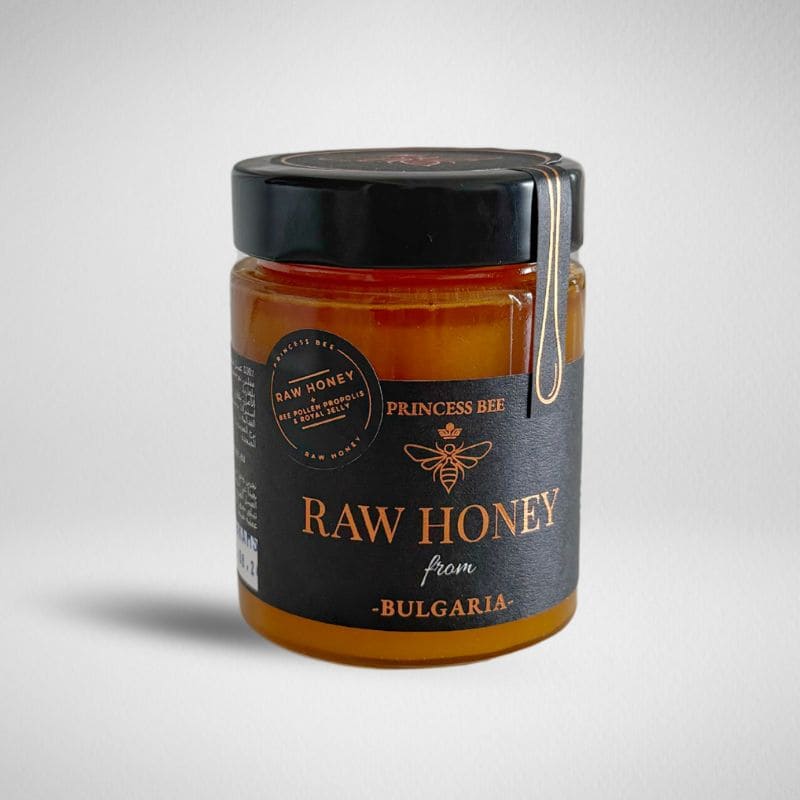 A jar of Princess Bee Raw Honey from Bulgaria, featuring a black lid and a black label with gold lettering and a bee logo, set against a light gray background.