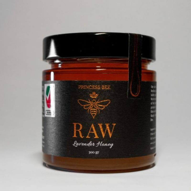 A jar of Princess Ber Raw Lavender Honey with a black lid and black label featuring gold lettering, set against a neutral gray background.