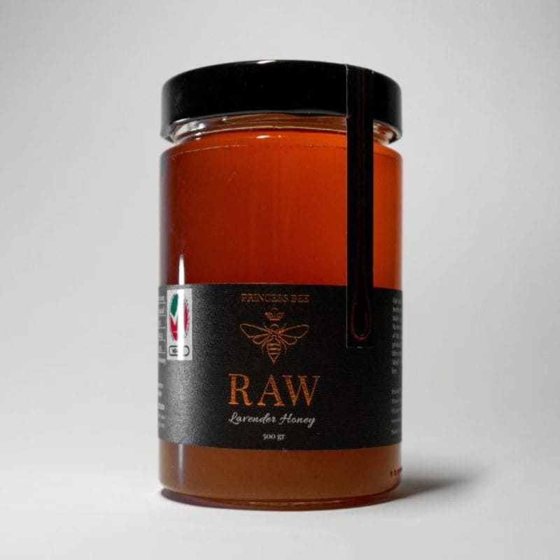 A jar of raw lavender honey with a black lid and black label, photographed on a neutral light gray background.