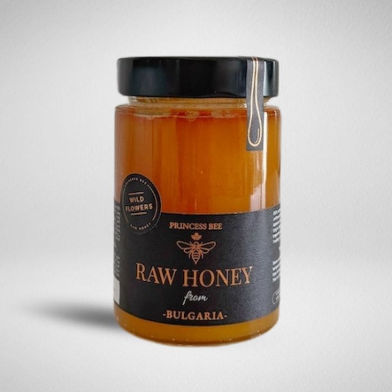 A glass jar of Princess Bee Raw Honey from Bulgaria, filled with golden amber honey and featuring a black label with gold lettering, set against a light gray background.