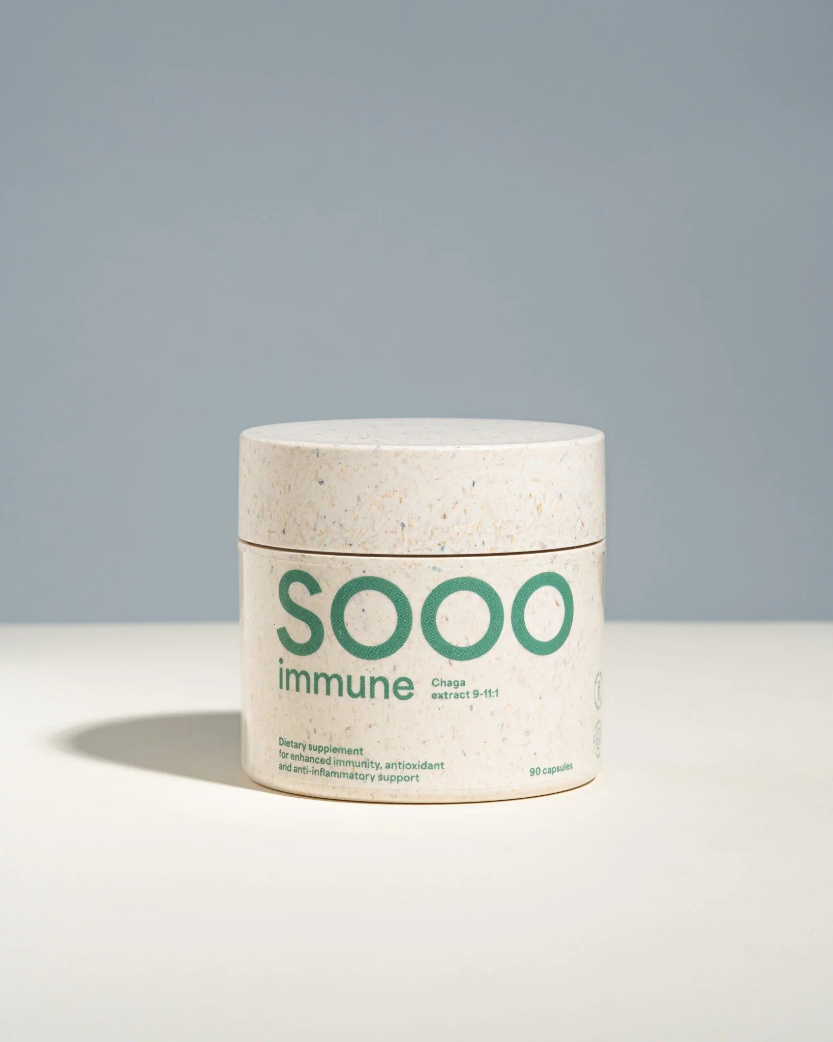 A white jar of SOOO Immune capsules with green text, set against a clean, two-toned gray and white background.