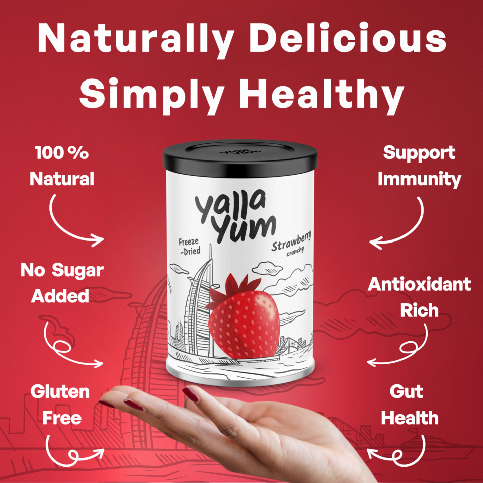 A canister of Yaja Yum Freeze-Dried Strawberries on a red promotional background with text highlighting natural, sugar-free, gluten-free benefits and a hand holding a strawberry below the product.