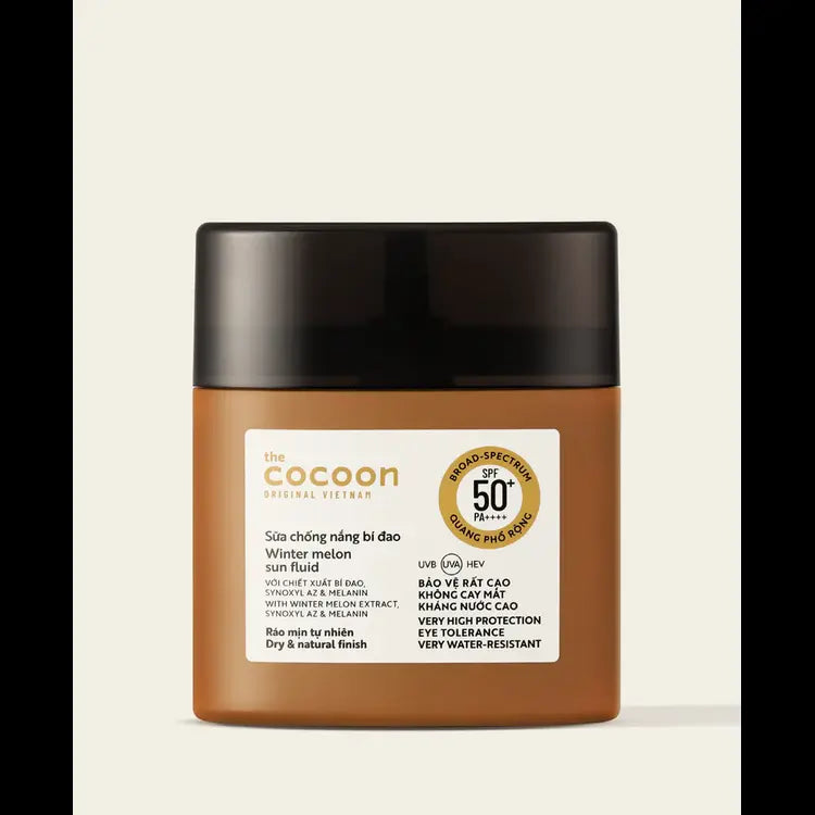 A jar of The Cocoon Sun Care Winter Melon Sun Block on a light beige background. The product is in a translucent amber-brown jar with a matte black lid and a white label featuring gold and black text.