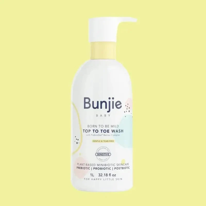 A bottle of Bunjie Baby Top to Toe Wash with a white pump dispenser and a pale yellow neck collar, set against a solid pale yellow background.