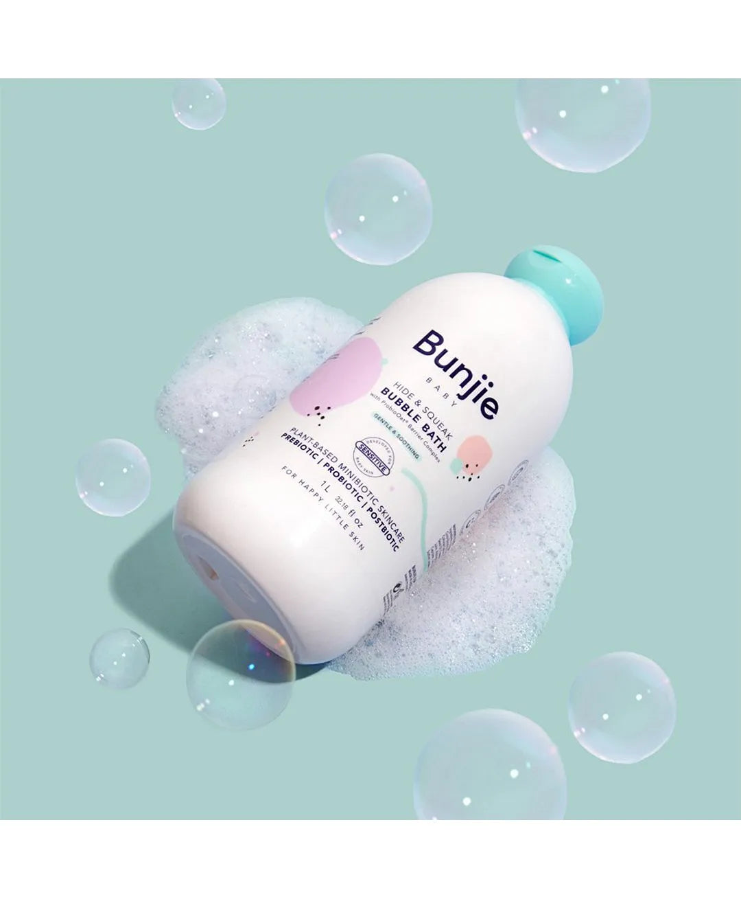 A bottle of Bunjie Baby & Kids Bubble & Bath wash with a turquoise cap, surrounded by white foam bubbles on a light teal background with floating soap bubbles.