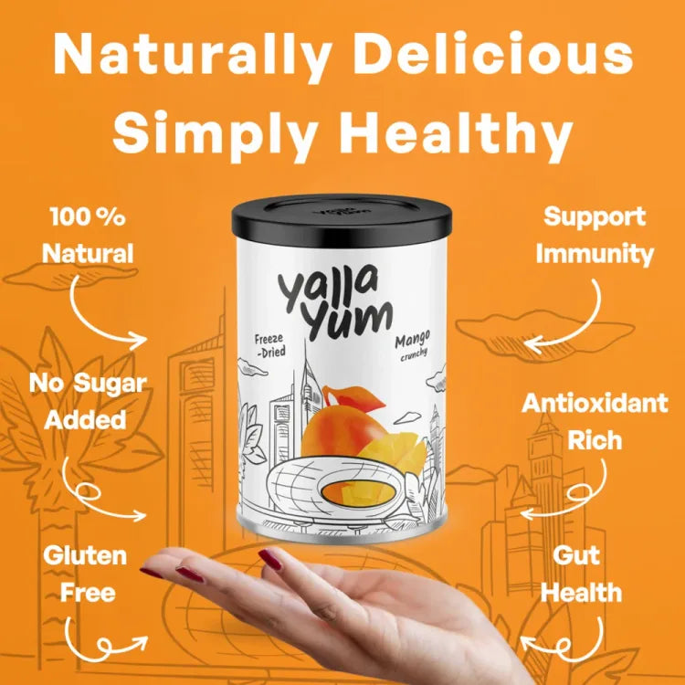 A canister of Yalla Yum freeze-dried mango crowflies is held in a hand against a bright orange background with promotional text highlighting its natural, sugar-free, gluten-free, and immune-supporting qualities.