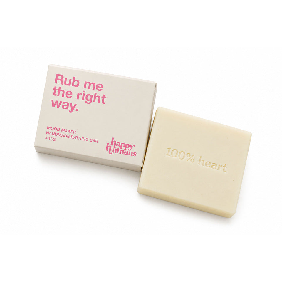 A cream-colored handmade bath bar next to its beige packaging box, which features pink text reading 'Rub me the right way.' and the brand name 'Happy Humans'.