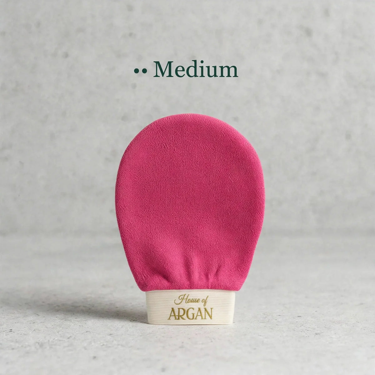 A pink massage brush head with a cream-colored base printed with 'House of ARGAN' in gold, set against a textured gray background with the text 'Medium' above.