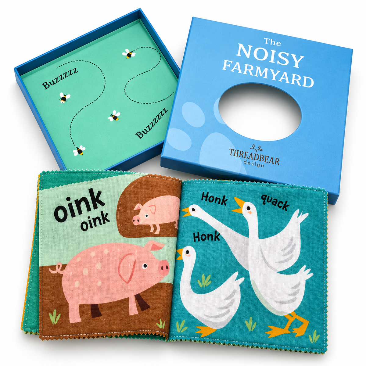 Threadbear 'The Noisy Farmyard' baby book set, showing the blue storage box, the open blue presentation tray with printed bee path, and the soft fabric book with colorful animal illustrations including a pink pig and white ducks.