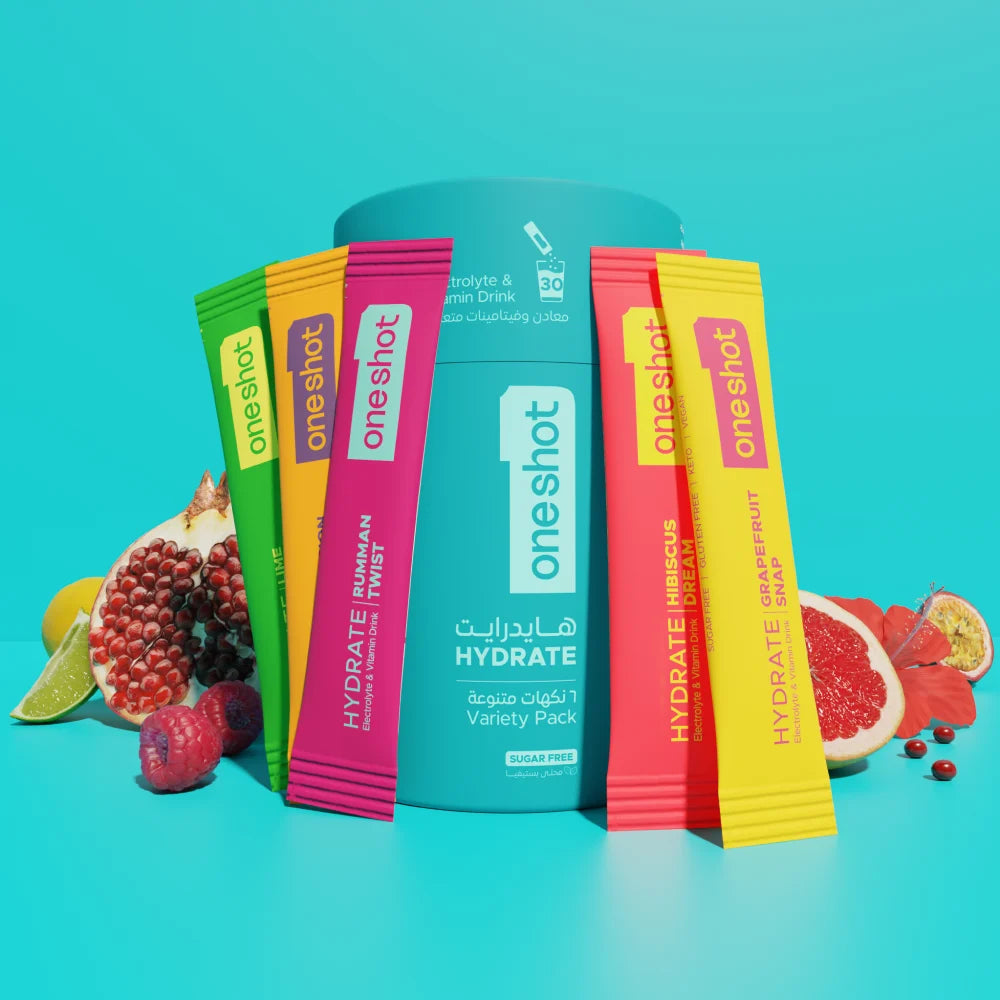 A set of OneShot Hydrate variety pack drink mix packets arranged around a large teal canister on a bright turquoise background, with fruit slices and whole fruits placed around them.