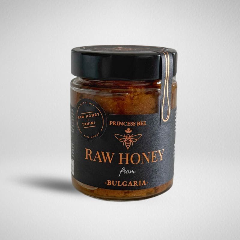 A glass jar of Princess Bee Raw Honey from Bulgaria, featuring a black lid with a gold hanging loop and a black label with gold lettering, set against a light gray background.