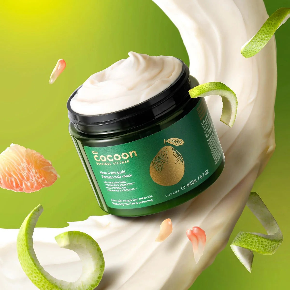 A jar of The Cocoon Natural Skincare Aloe 3-in-1 Body Butter with whipped cream visible at the top, set against a dynamic green and white splash background with floating aloe vera slices and grapefruit pieces.